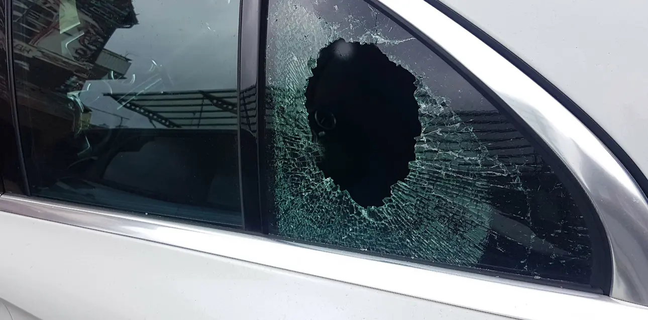 Die kaputte Fensterscheibe eines Autos. Sie ist zersplittert und hat ein Loch.