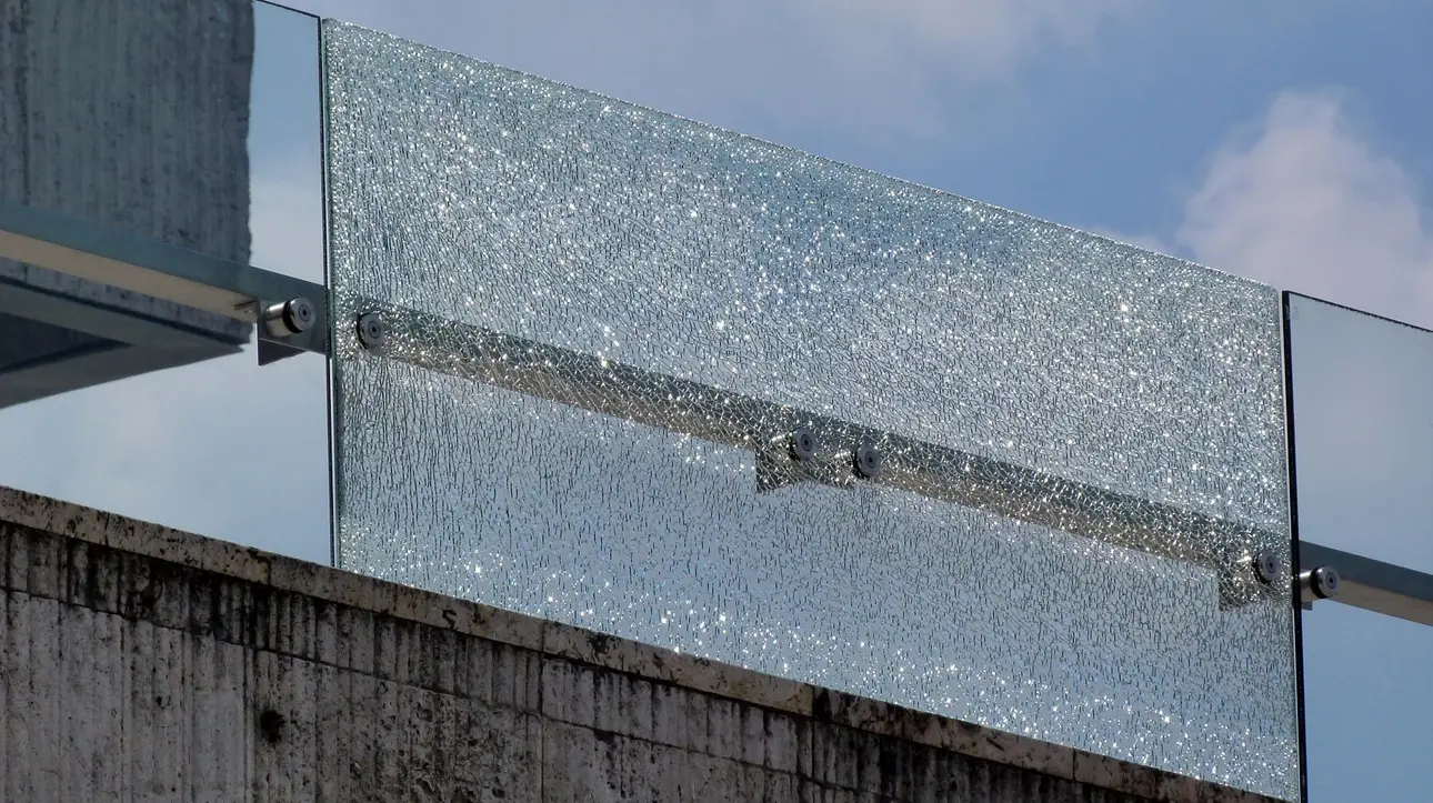 Die gesprungene Glasscheibe einer Fassade, die durch eine Schutzfolie noch zusammengehalten wird.